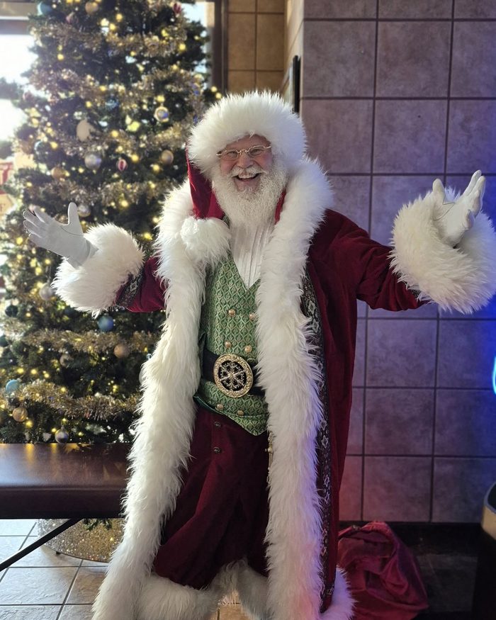 Santa in his regal burgundy robe and green vest, arms open in welcome