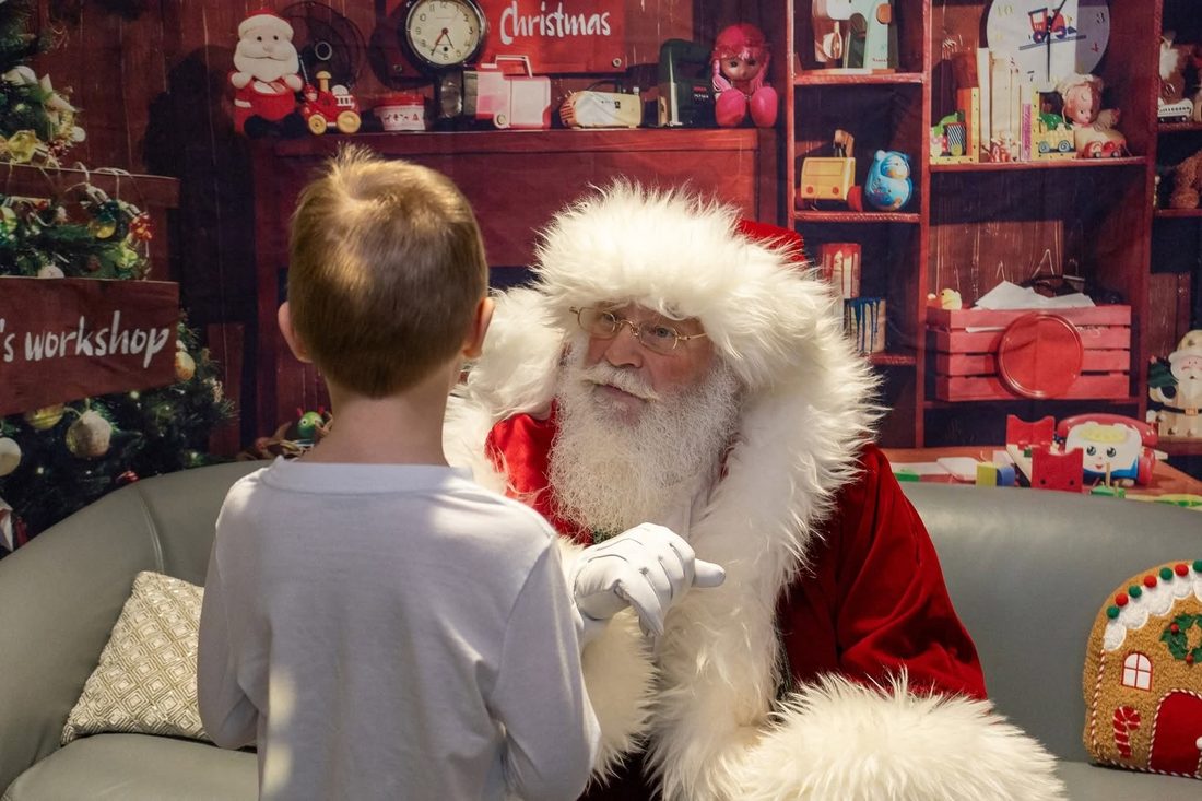 Santa blowing magic snow with three delighted children in front of the Christmas trees